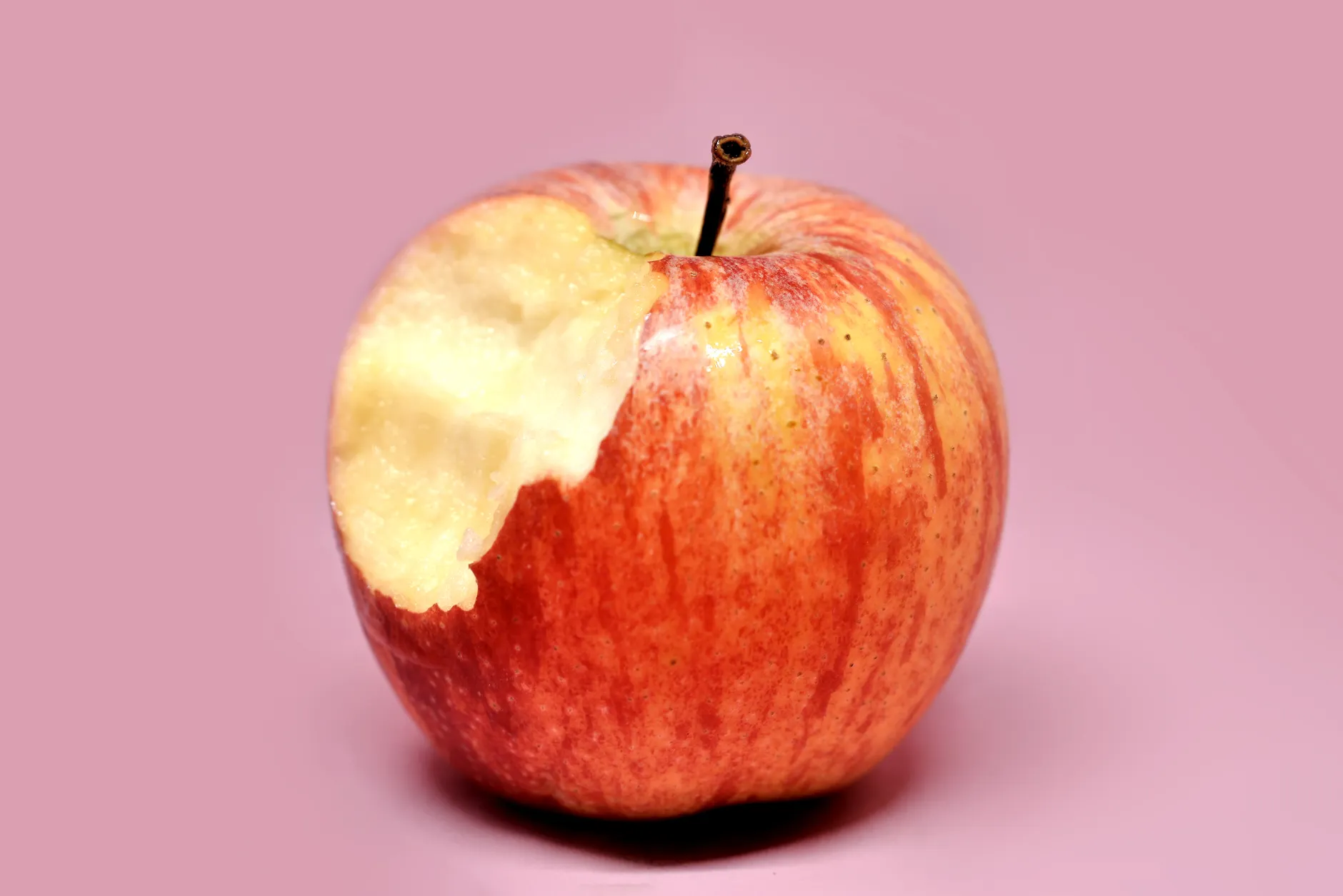Close-up of a red apple with a bite taken, isolated on a pink background.