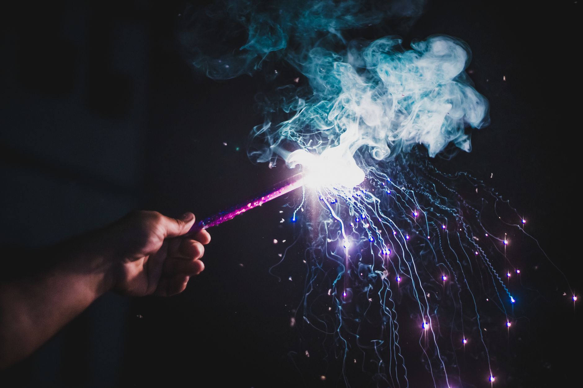 Crop anonymous person standing on street and demonstrating burning sparkling candle against dark night sky