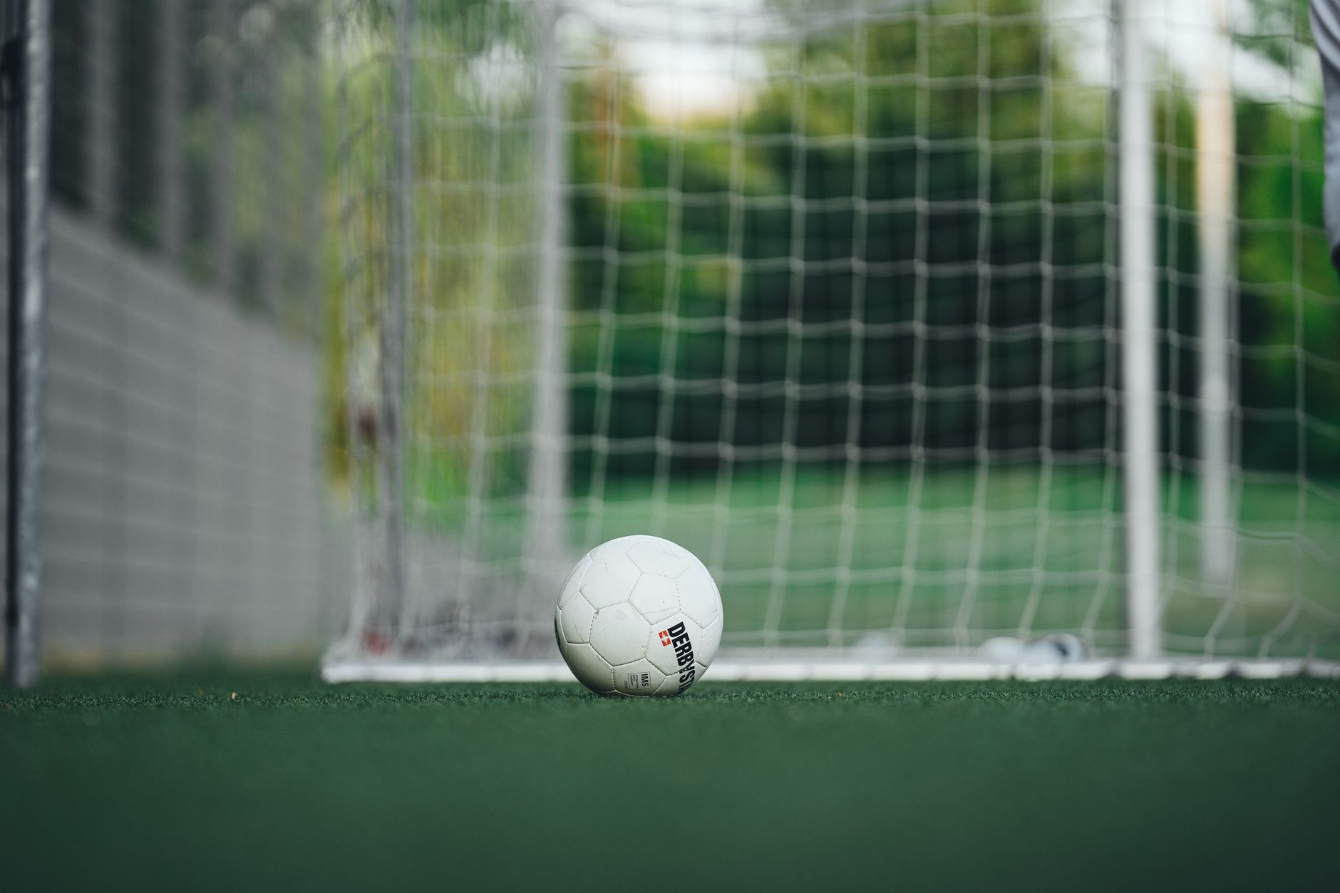 Close-up of soccer ball on outdoor field with goal net, perfect for sports themes.