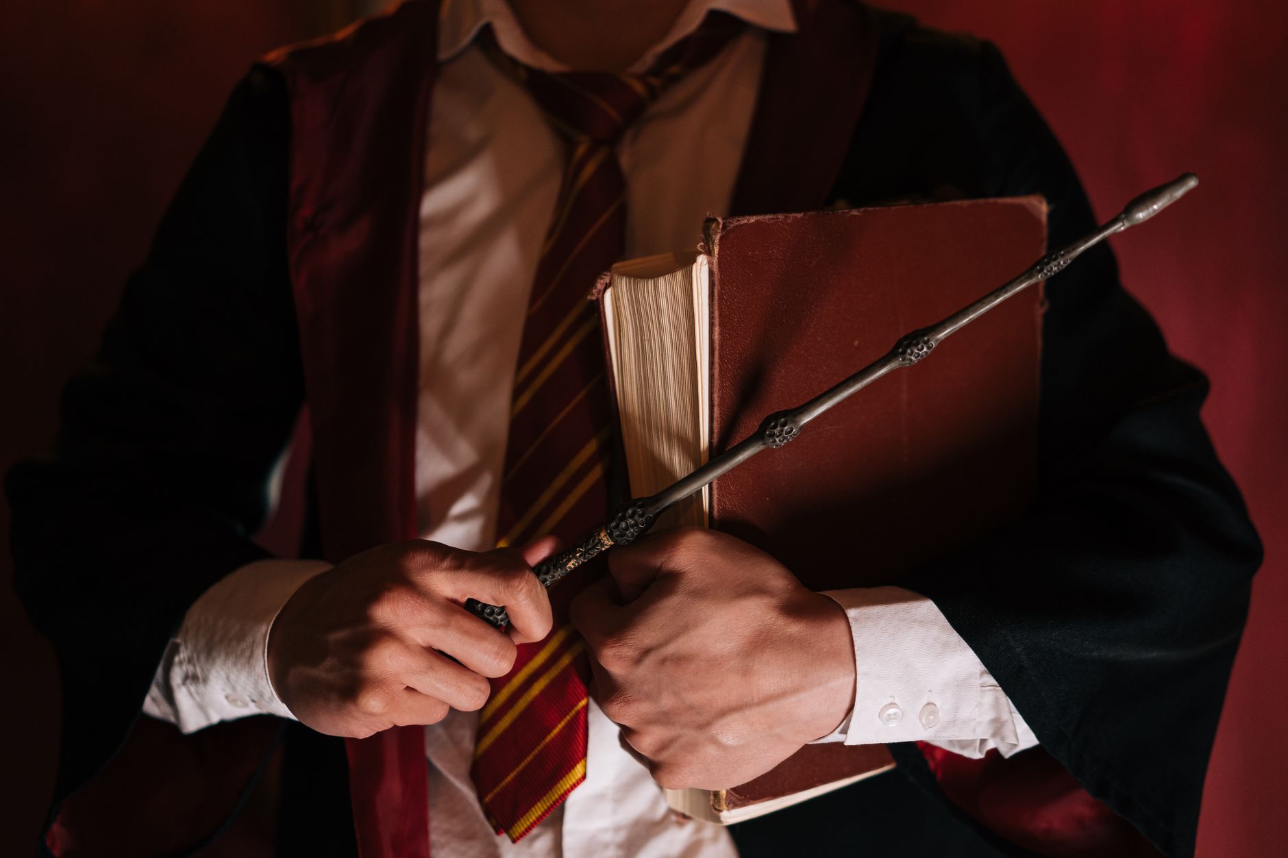 Close-up of a person holding a spell book and wand, evoking wizardry and magic.