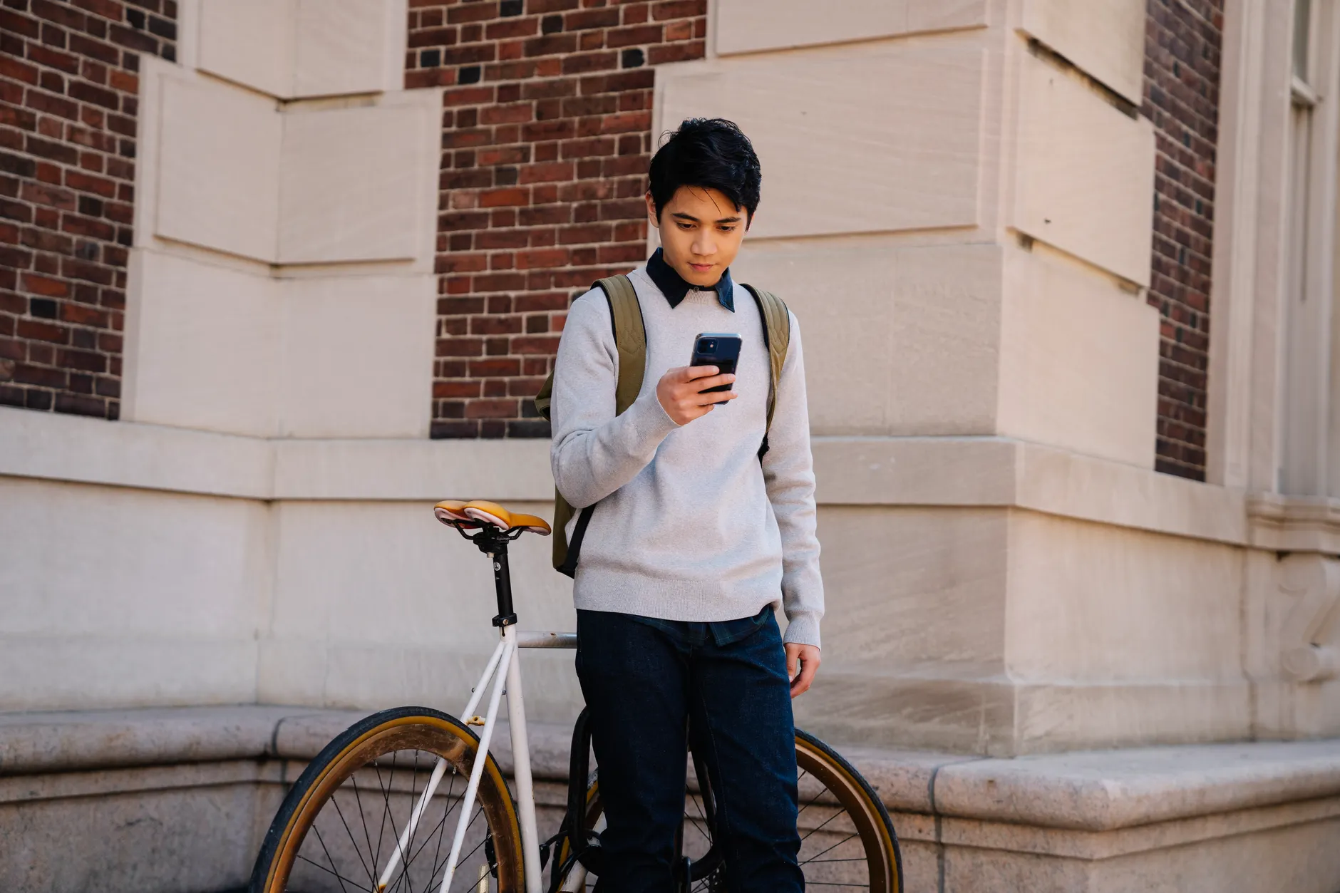 Young man with a smartphone next to a bicycle against a brick wall.