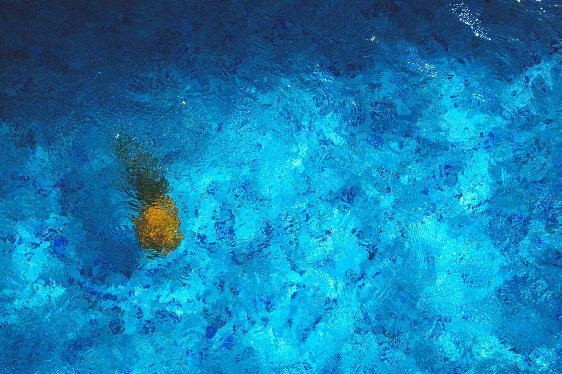 A pineapple submerged in a vibrant blue pool creates a tropical abstract scene.