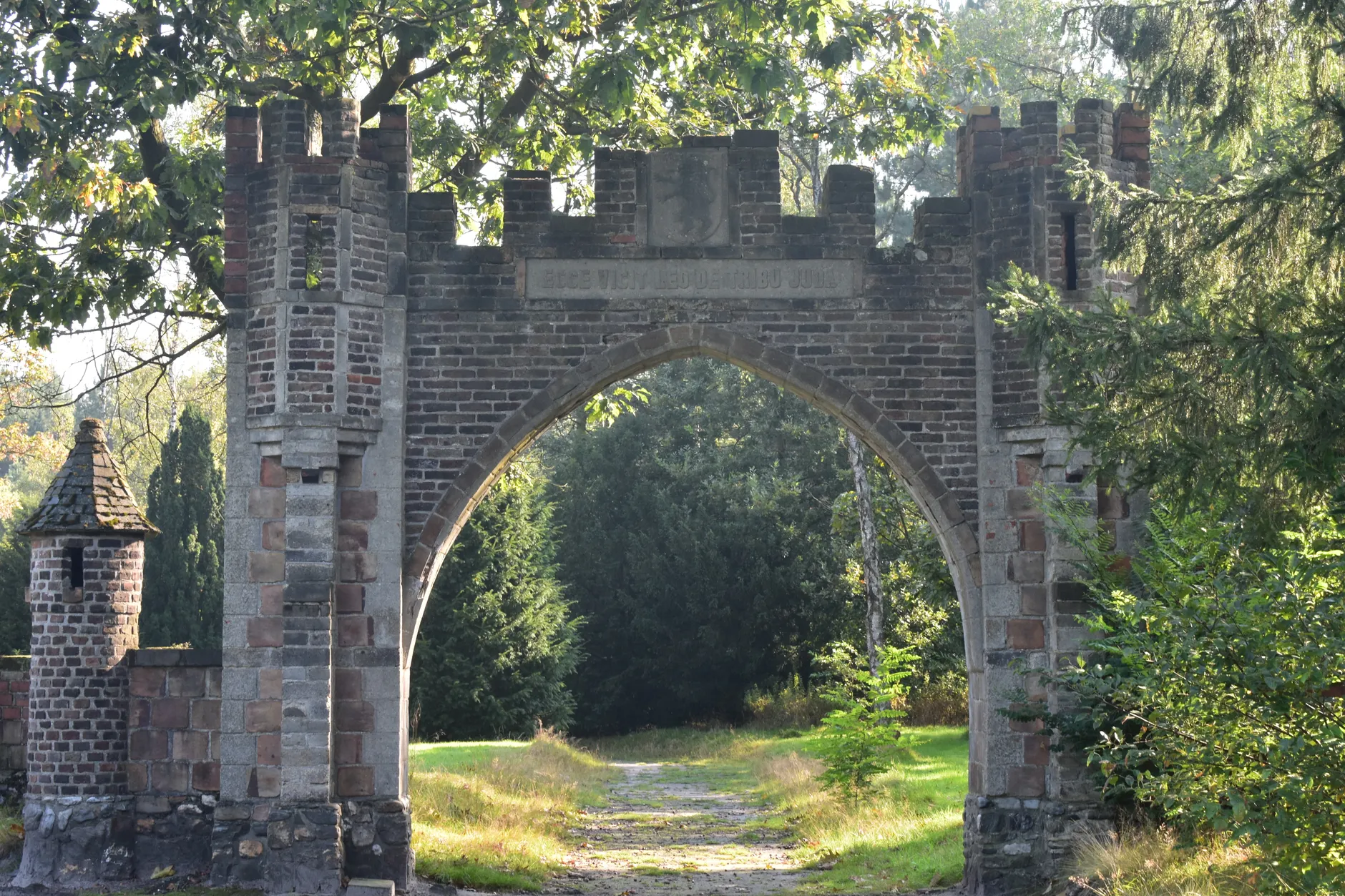 A historic brick gate stands amidst dense greenery, capturing architectural beauty.