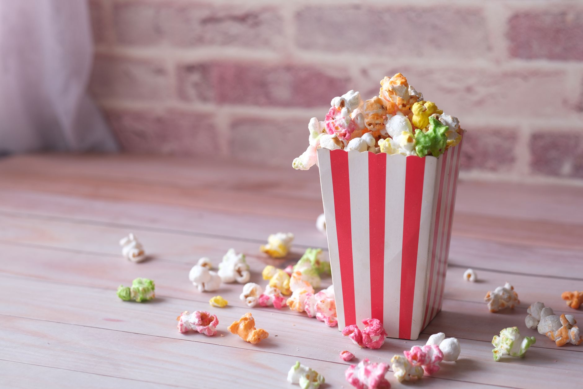 A vibrant shot of multicolored popcorn spilling from a striped box on a wooden table.